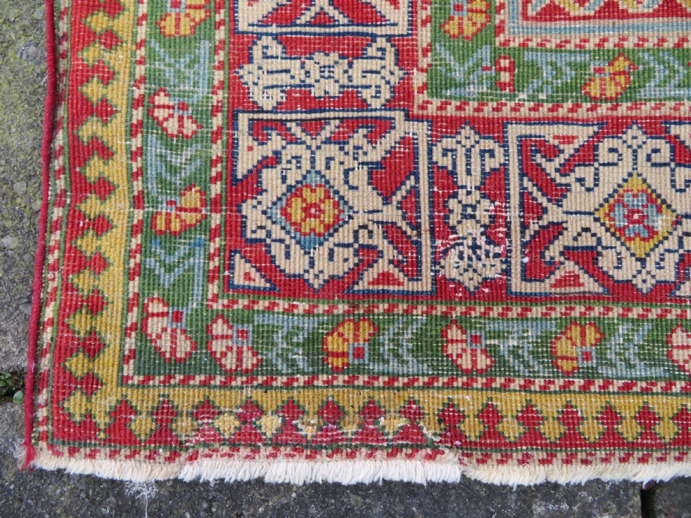 An antique hand-knotted Caucasian rug featuring a distressed yellow central field patterned with geometric ram horn motifs framed by red and green decorative borders. View XV