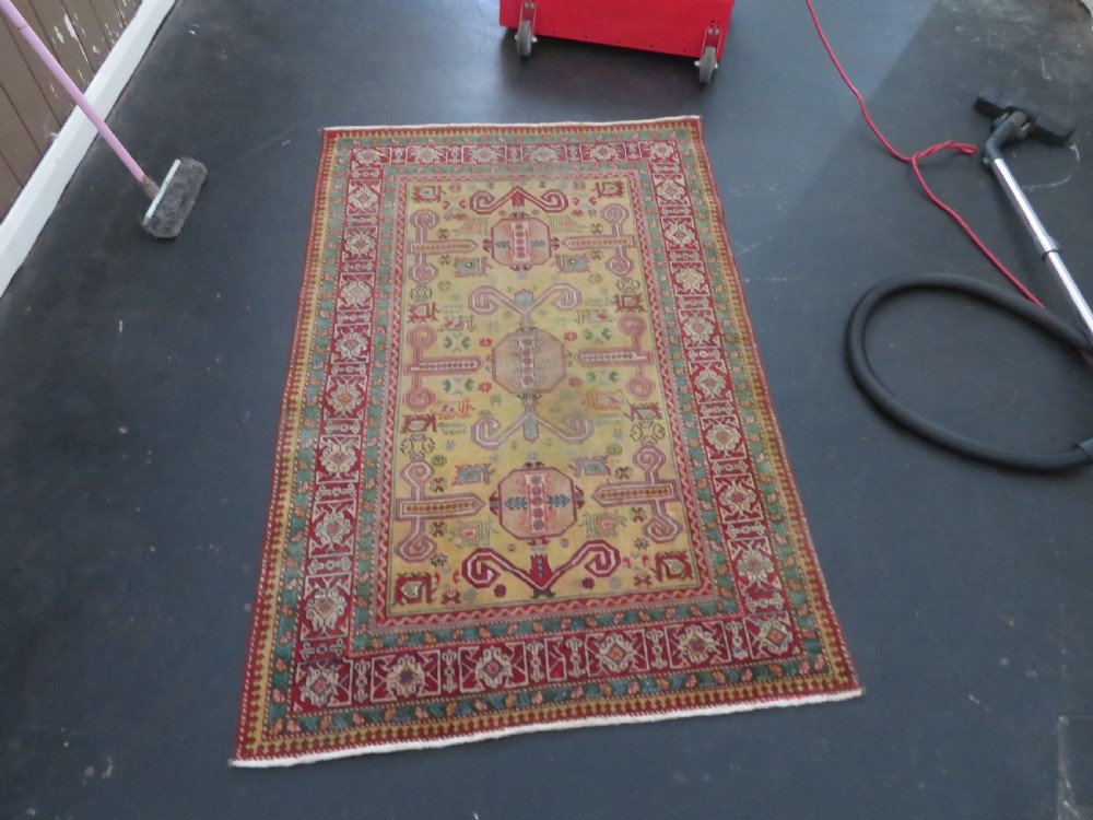 An antique hand-knotted Caucasian rug featuring a distressed yellow central field patterned with geometric ram horn motifs framed by red and green decorative borders. View XXI