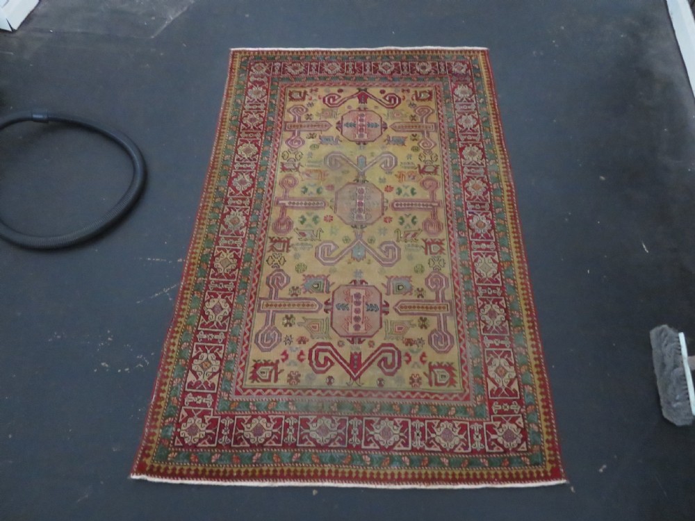 An antique hand-knotted Caucasian rug featuring a distressed yellow central field patterned with geometric ram horn motifs framed by red and green decorative borders. View XXII
