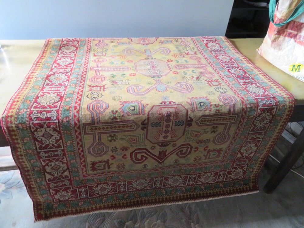 An antique hand-knotted Caucasian rug featuring a distressed yellow central field patterned with geometric ram horn motifs framed by red and green decorative borders. View XXIII