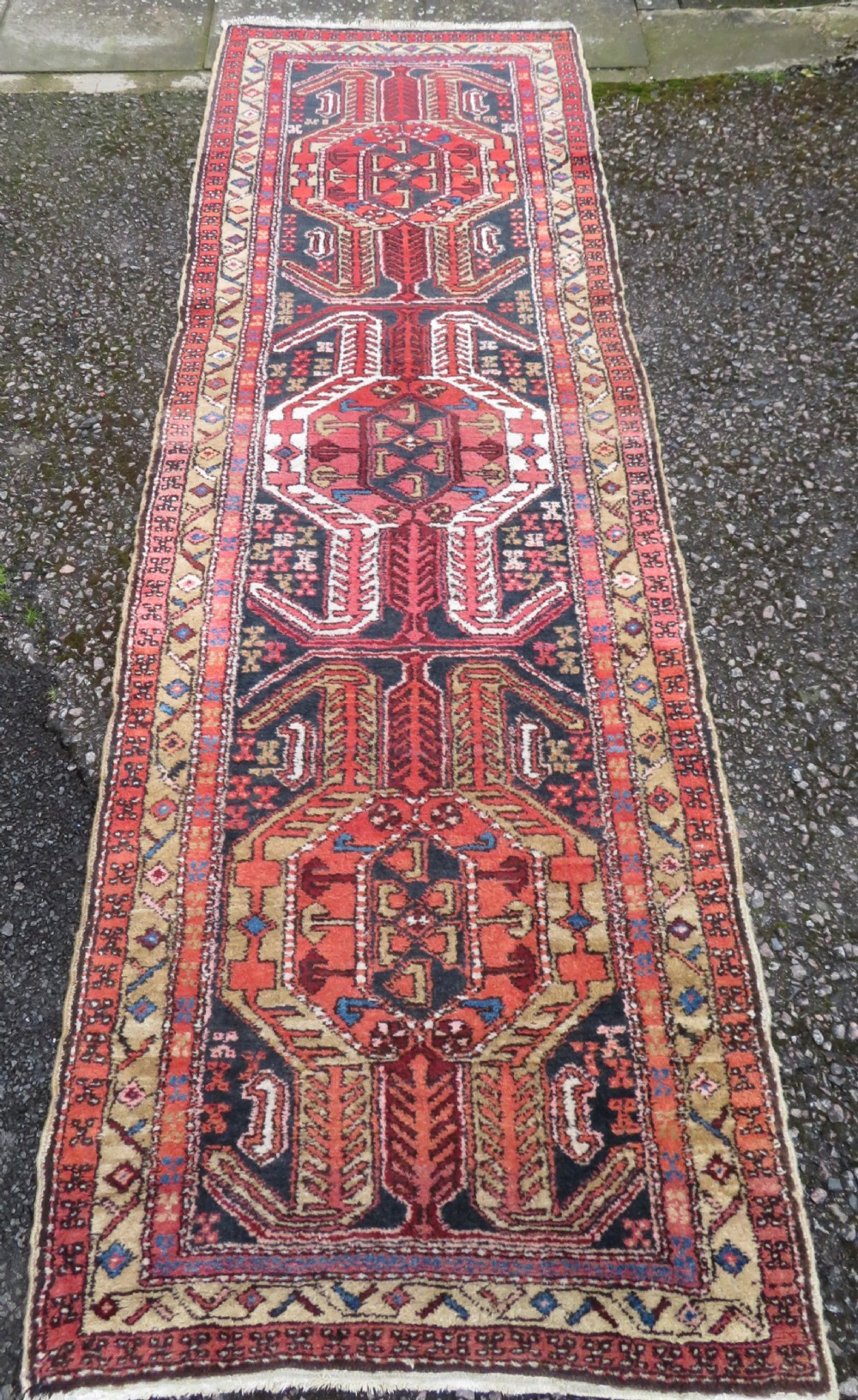 A long hand-knotted Persian Heriz runner rug featuring central geometric medallions in terracotta red and navy blue bordered by intricate geometric patterns.