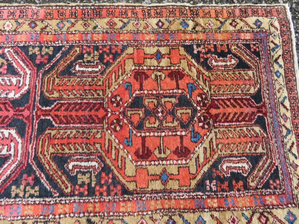 A long hand-knotted Persian Heriz runner rug featuring central geometric medallions in terracotta red and navy blue bordered by intricate geometric patterns. View IV