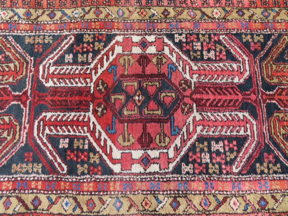 A long hand-knotted Persian Heriz runner rug featuring central geometric medallions in terracotta red and navy blue bordered by intricate geometric patterns. View V
