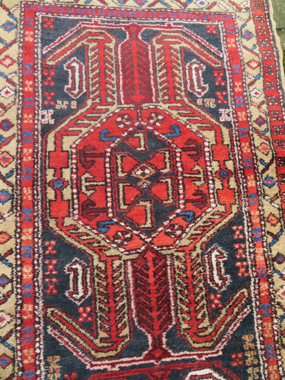 A long hand-knotted Persian Heriz runner rug featuring central geometric medallions in terracotta red and navy blue bordered by intricate geometric patterns. View X