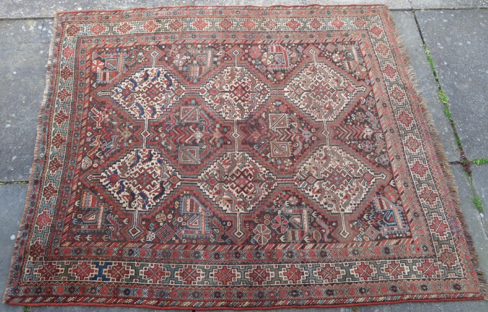 A rectangular hand-knotted antique Khamseh wool rug featuring geometric diamond medallions and intricate border patterns in terracotta, dark brown, and cream. View III