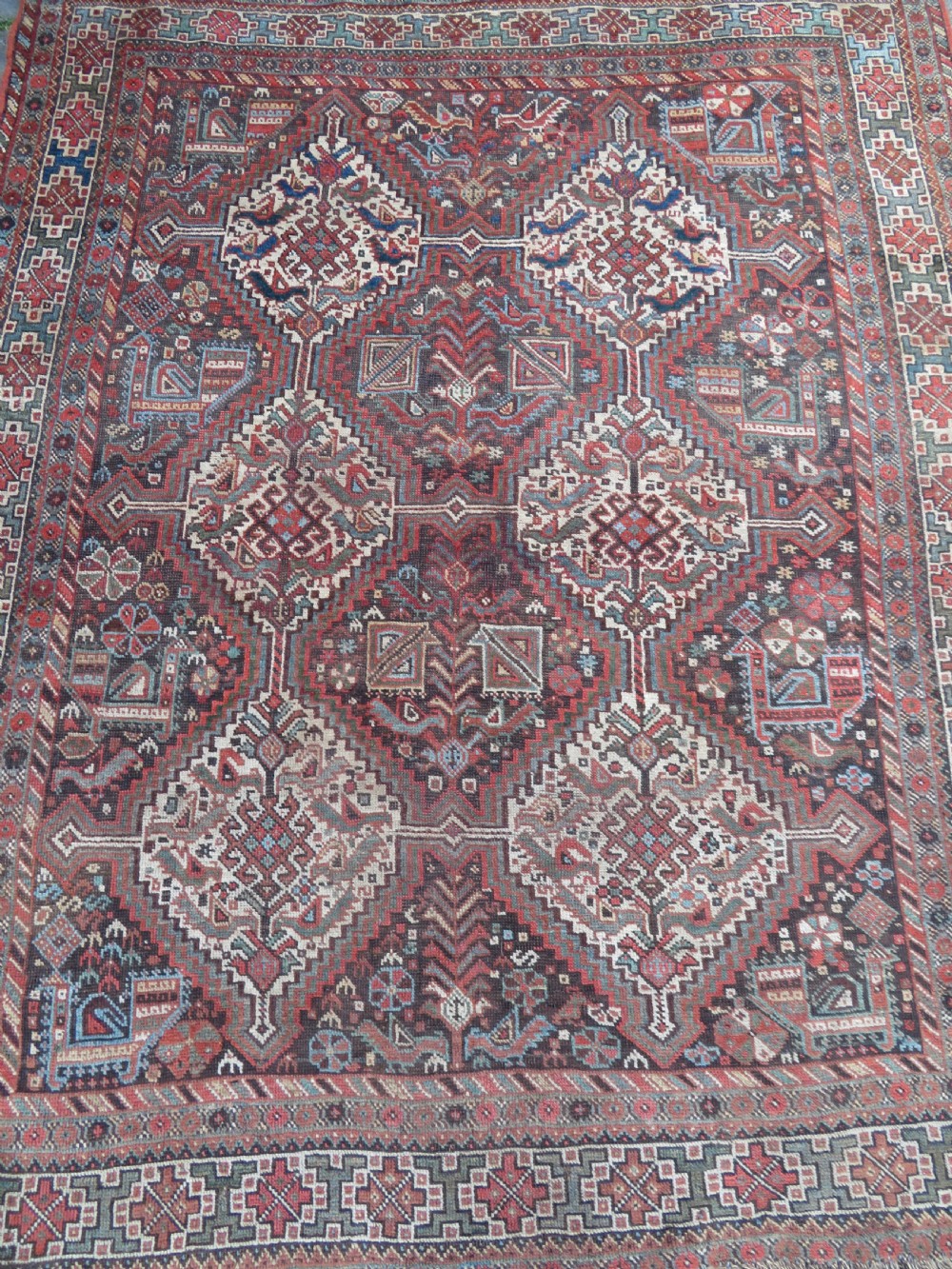 A rectangular hand-knotted antique Khamseh wool rug featuring geometric diamond medallions and intricate border patterns in terracotta, dark brown, and cream. View IV