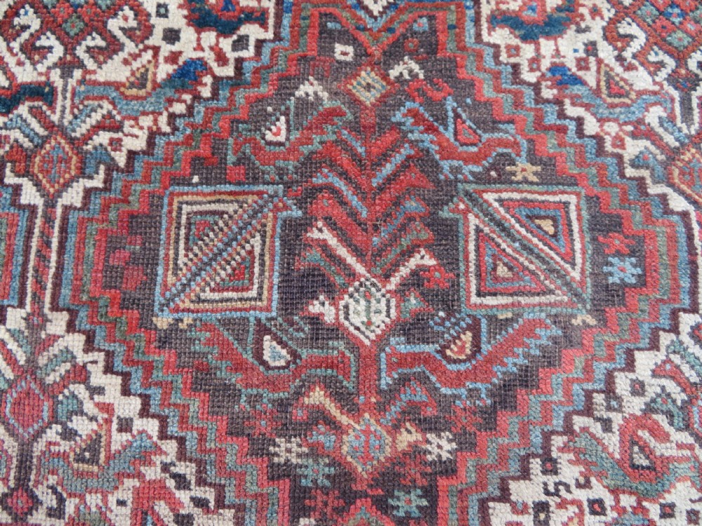 A rectangular hand-knotted antique Khamseh wool rug featuring geometric diamond medallions and intricate border patterns in terracotta, dark brown, and cream. View V