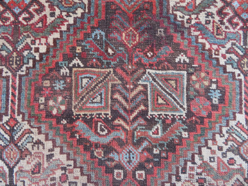 A rectangular hand-knotted antique Khamseh wool rug featuring geometric diamond medallions and intricate border patterns in terracotta, dark brown, and cream. View VI