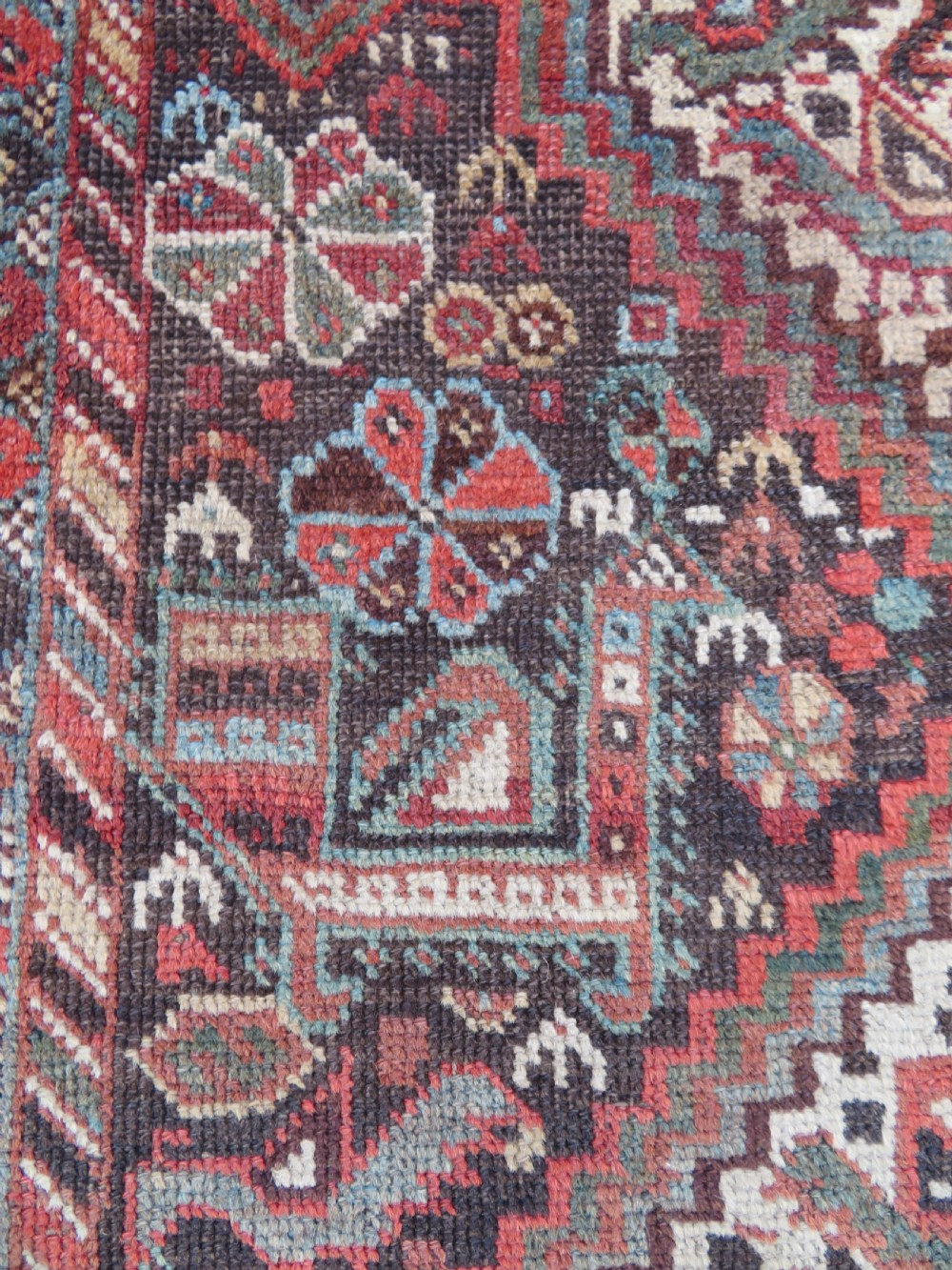 A rectangular hand-knotted antique Khamseh wool rug featuring geometric diamond medallions and intricate border patterns in terracotta, dark brown, and cream. View VIII