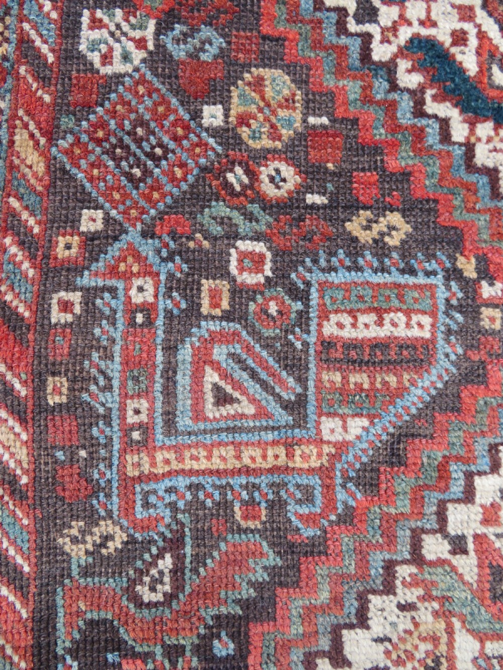 A rectangular hand-knotted antique Khamseh wool rug featuring geometric diamond medallions and intricate border patterns in terracotta, dark brown, and cream. View IX