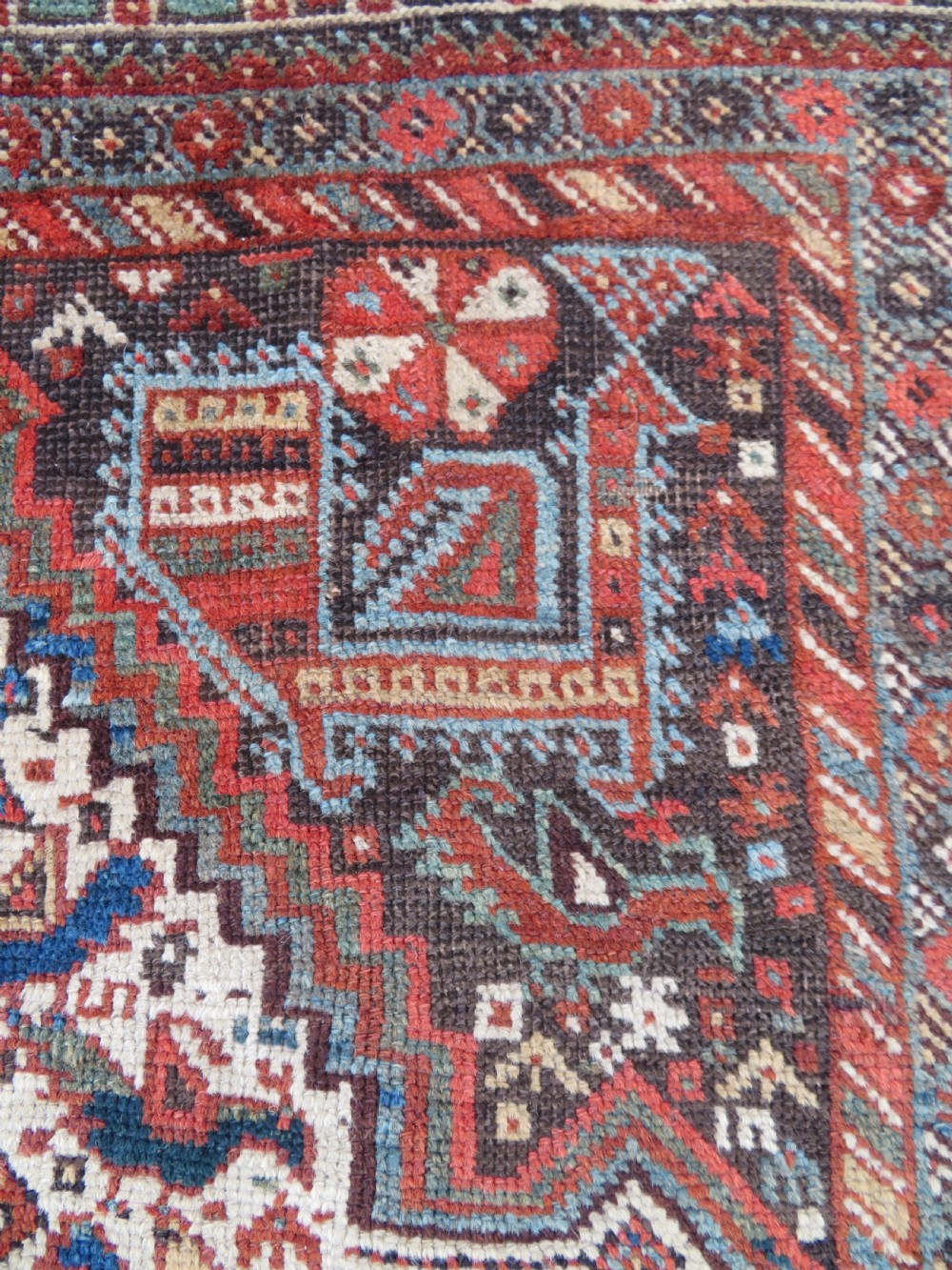 A rectangular hand-knotted antique Khamseh wool rug featuring geometric diamond medallions and intricate border patterns in terracotta, dark brown, and cream. View X