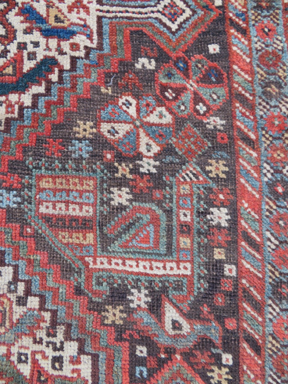 A rectangular hand-knotted antique Khamseh wool rug featuring geometric diamond medallions and intricate border patterns in terracotta, dark brown, and cream. View XI