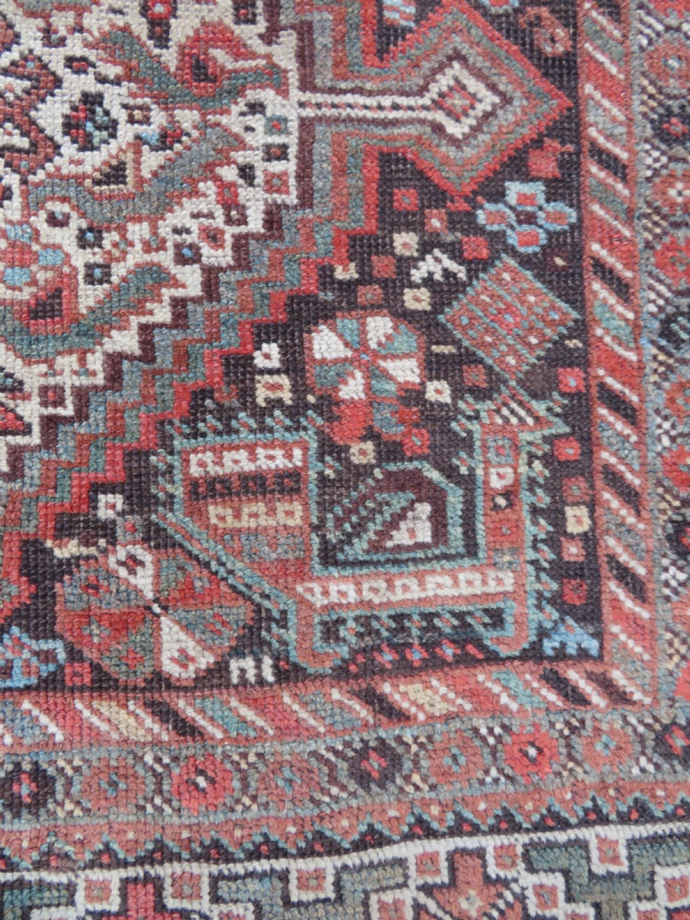 A rectangular hand-knotted antique Khamseh wool rug featuring geometric diamond medallions and intricate border patterns in terracotta, dark brown, and cream. View XIII