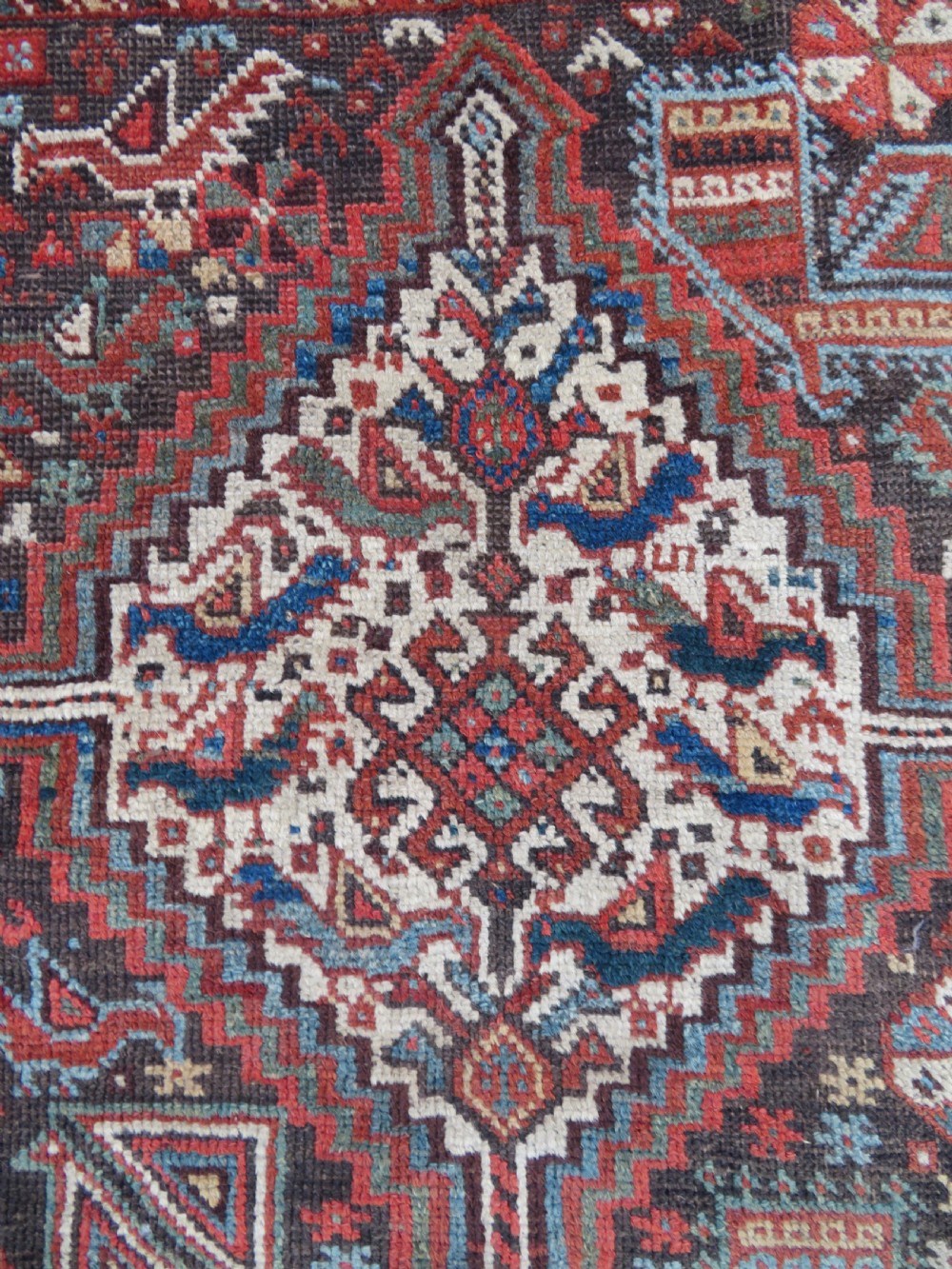 A rectangular hand-knotted antique Khamseh wool rug featuring geometric diamond medallions and intricate border patterns in terracotta, dark brown, and cream. View XV