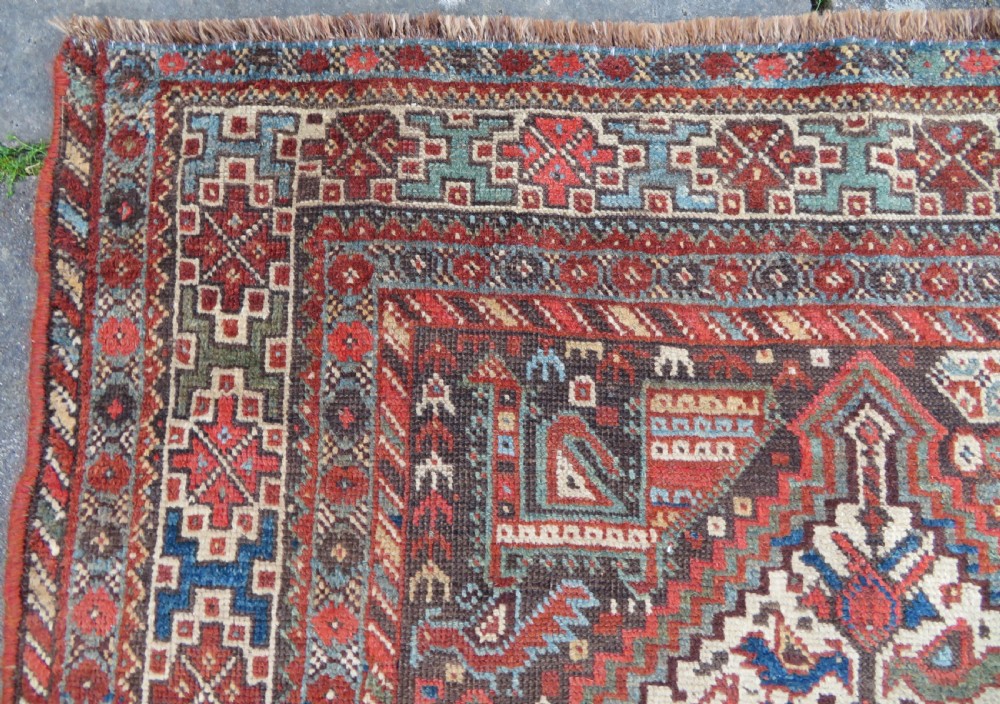 A rectangular hand-knotted antique Khamseh wool rug featuring geometric diamond medallions and intricate border patterns in terracotta, dark brown, and cream. View XVI