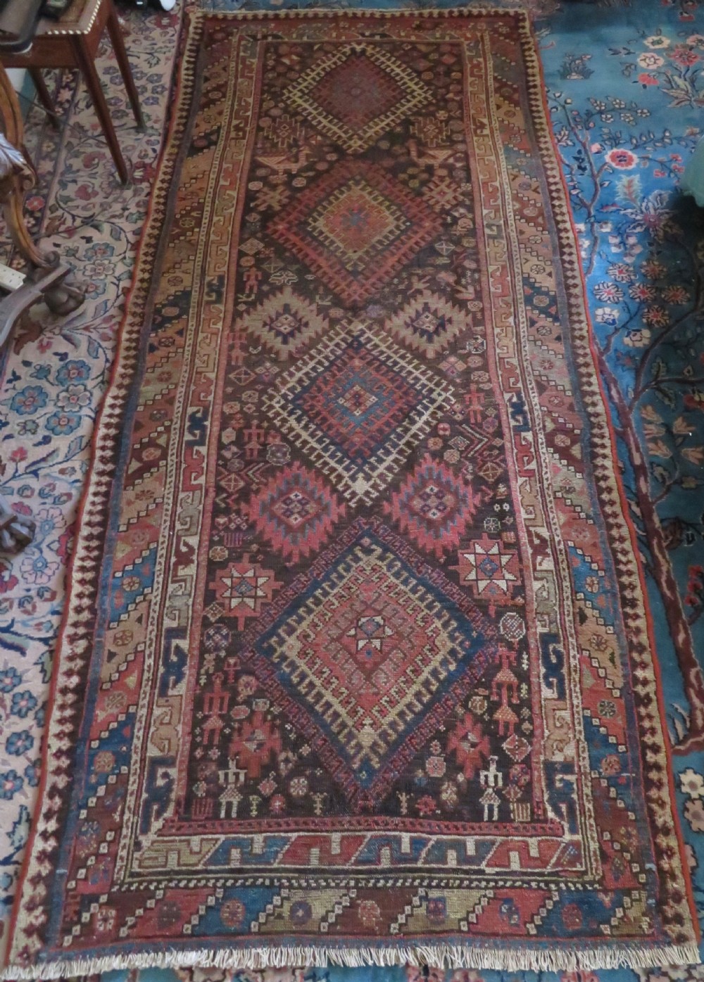 An antique hand-knotted wool runner rug featuring repeating geometric diamond medallions down a central dark field with multi-tiered tribal borders.