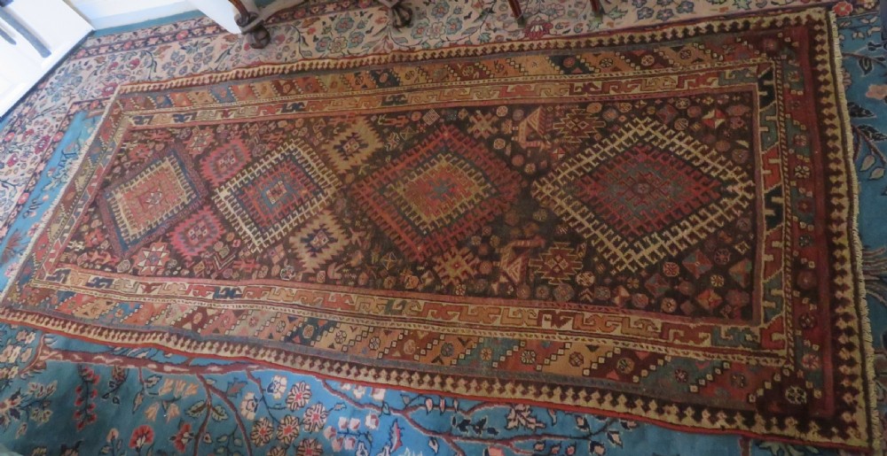 An antique hand-knotted wool runner rug featuring repeating geometric diamond medallions down a central dark field with multi-tiered tribal borders. View II