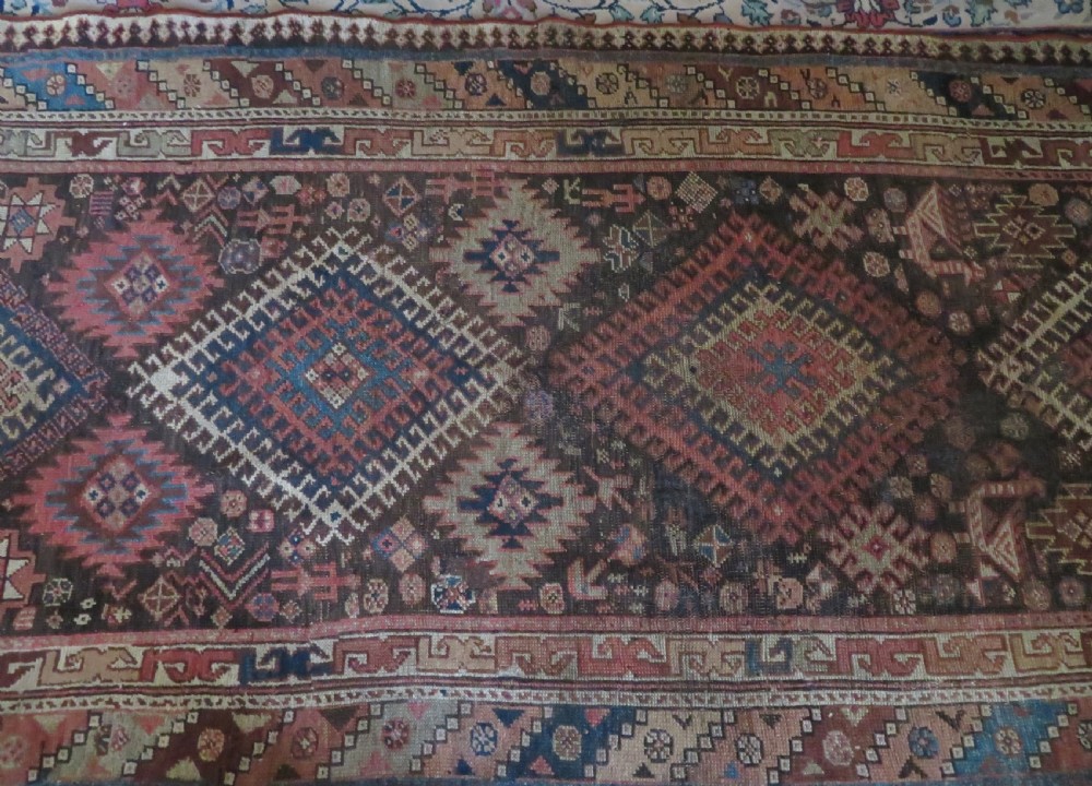 An antique hand-knotted wool runner rug featuring repeating geometric diamond medallions down a central dark field with multi-tiered tribal borders. View III