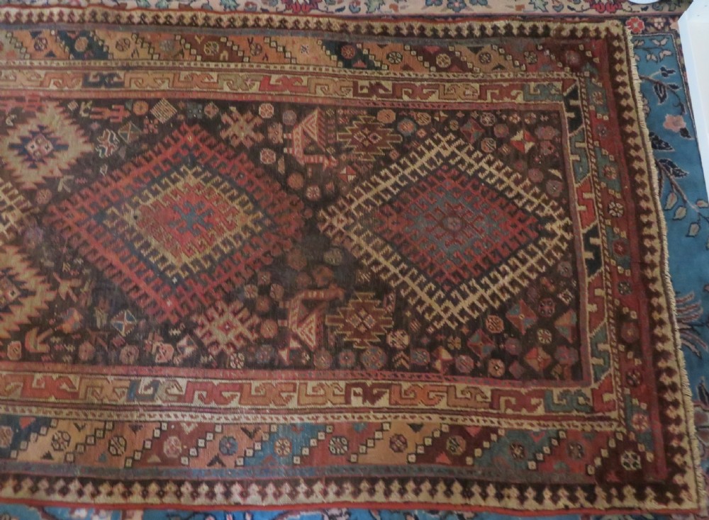 An antique hand-knotted wool runner rug featuring repeating geometric diamond medallions down a central dark field with multi-tiered tribal borders. View IV