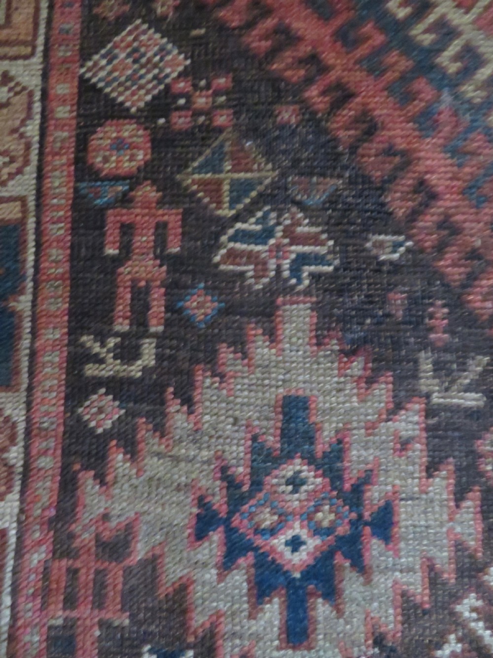 An antique hand-knotted wool runner rug featuring repeating geometric diamond medallions down a central dark field with multi-tiered tribal borders. View IX