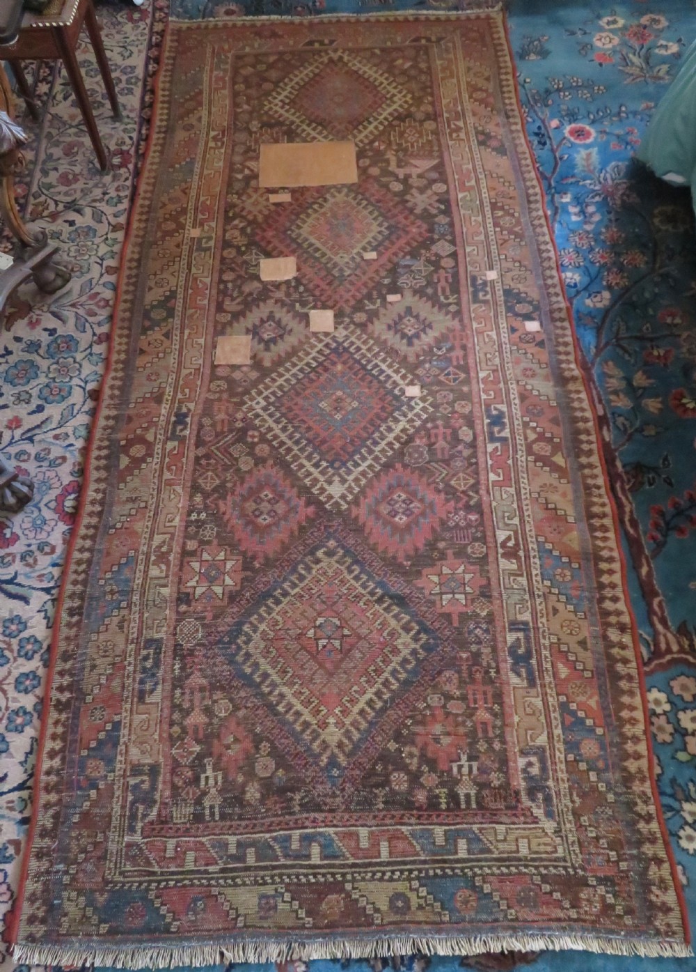An antique hand-knotted wool runner rug featuring repeating geometric diamond medallions down a central dark field with multi-tiered tribal borders. View XXI