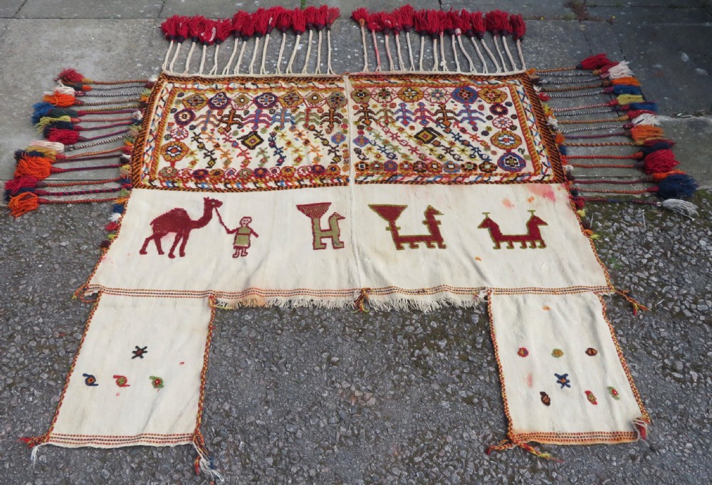 An antique cream handwoven wool Qashqai horse cover featuring colourful geometric patterns, human and camel motifs, and decorative edge tassels.