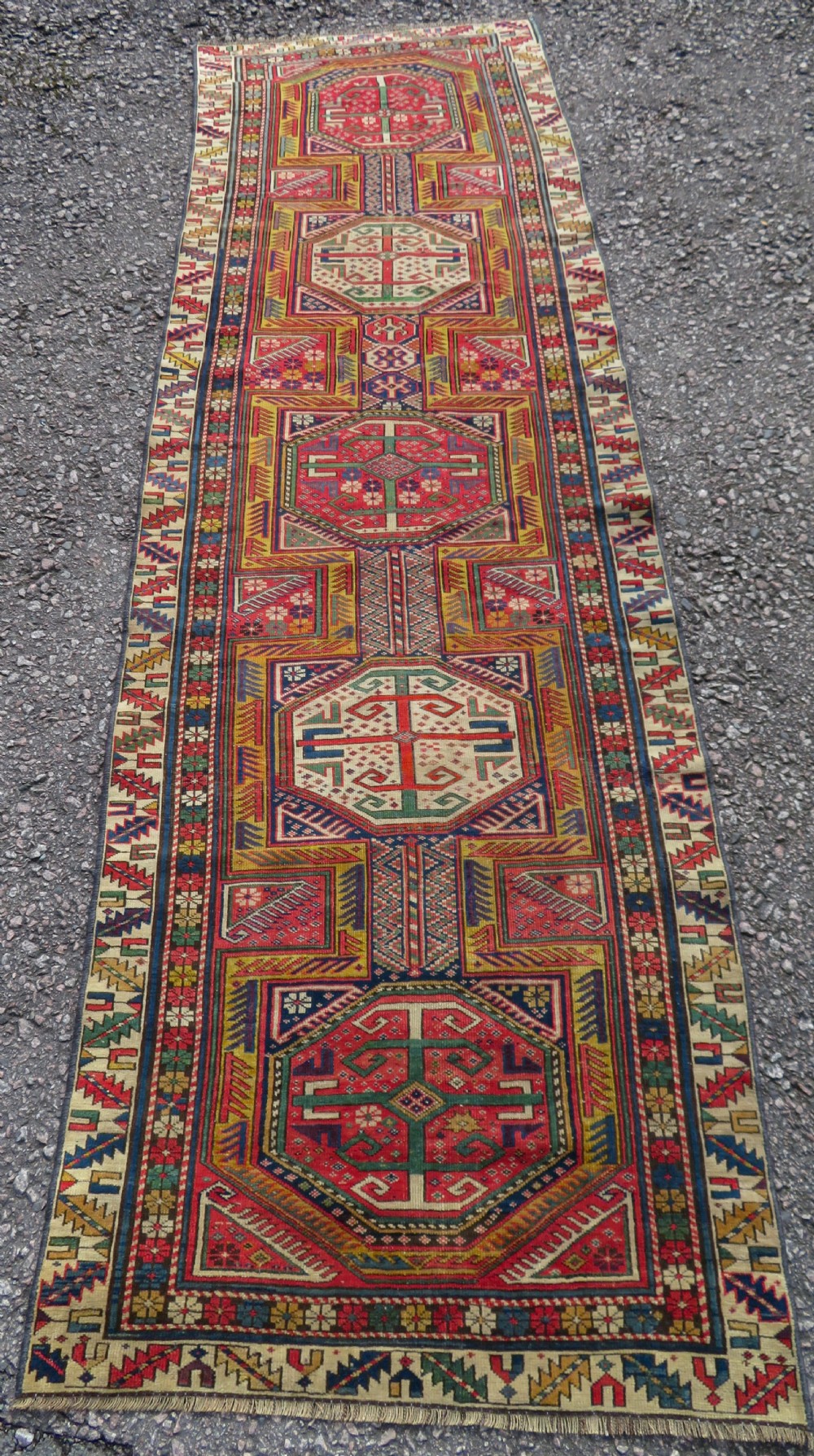 An antique Caucasian Shirvan wool runner rug with repeating geometric octagonal medallions framed by intricate multi-coloured borders.