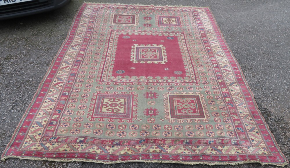 An antique Turkish Bergama wool carpet featuring a red central field surrounded by sage green areas with geometric Holbein square medallions and detailed borders.