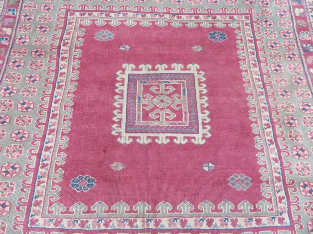An antique Turkish Bergama wool carpet featuring a red central field surrounded by sage green areas with geometric Holbein square medallions and detailed borders. View IV
