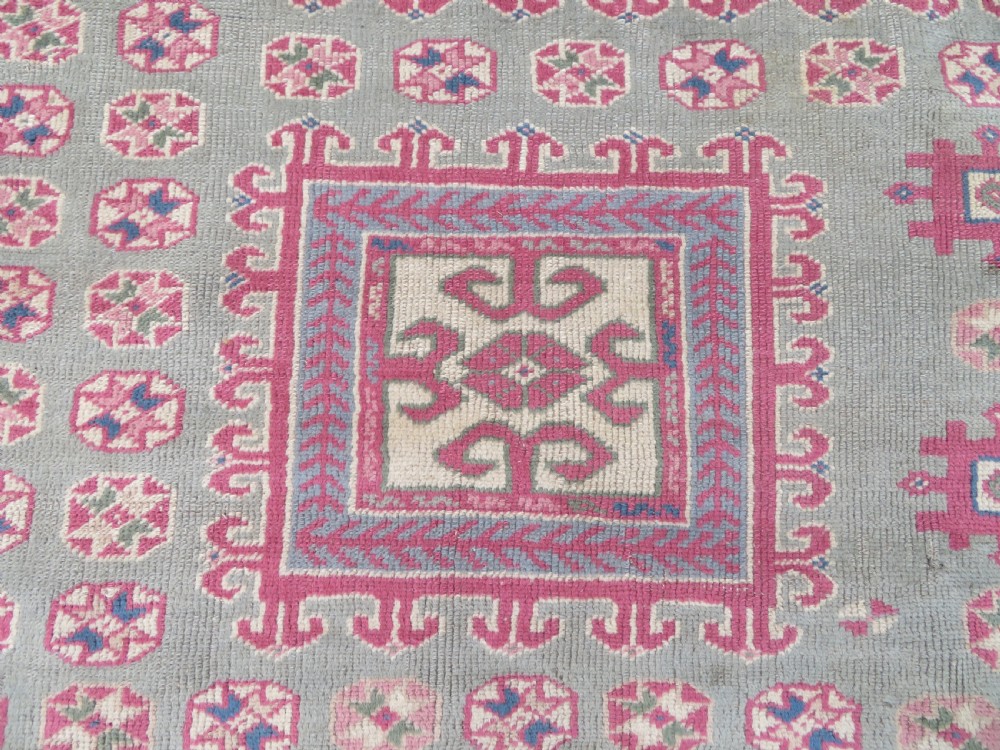 An antique Turkish Bergama wool carpet featuring a red central field surrounded by sage green areas with geometric Holbein square medallions and detailed borders. View VI