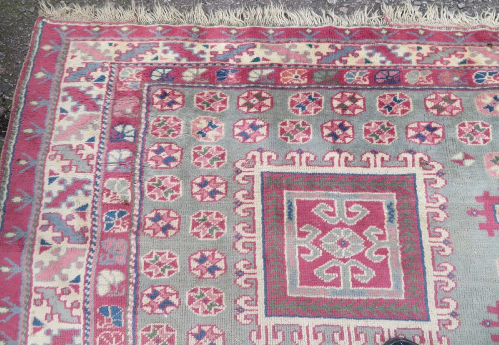 An antique Turkish Bergama wool carpet featuring a red central field surrounded by sage green areas with geometric Holbein square medallions and detailed borders. View IX