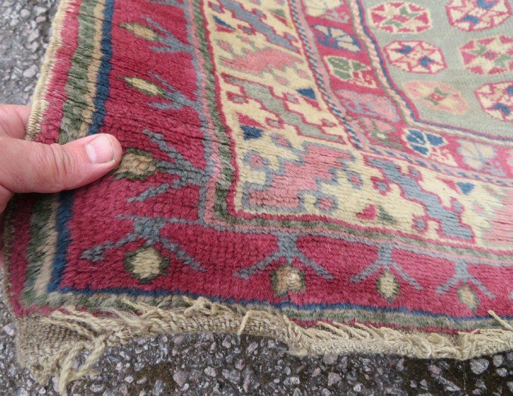 An antique Turkish Bergama wool carpet featuring a red central field surrounded by sage green areas with geometric Holbein square medallions and detailed borders. View XIII