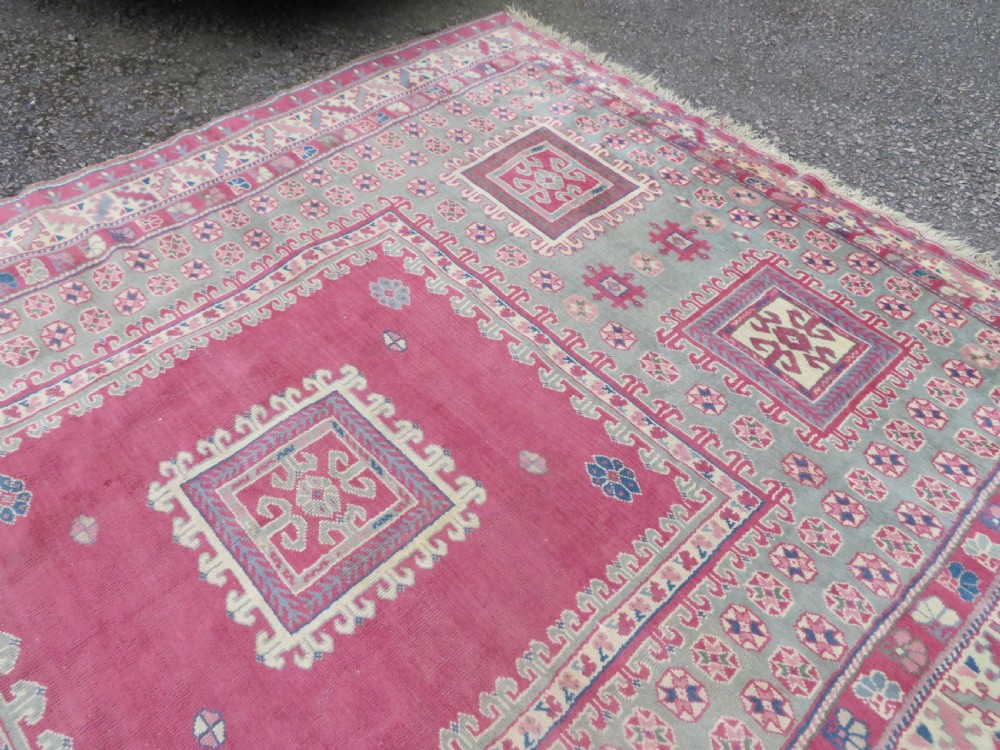 An antique Turkish Bergama wool carpet featuring a red central field surrounded by sage green areas with geometric Holbein square medallions and detailed borders. View XVII