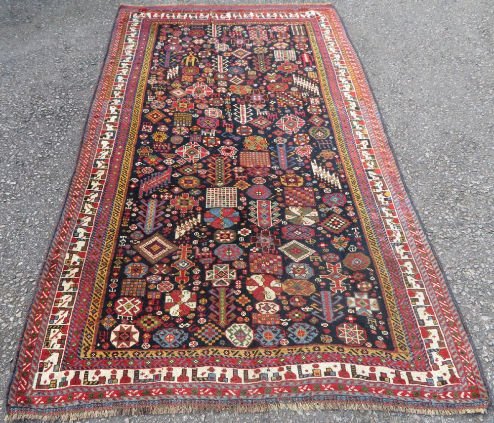 An antique hand-knotted Qashqai wool rug featuring a dark navy field densely filled with geometric tribal motifs and stylised figures within a multi-tiered border.