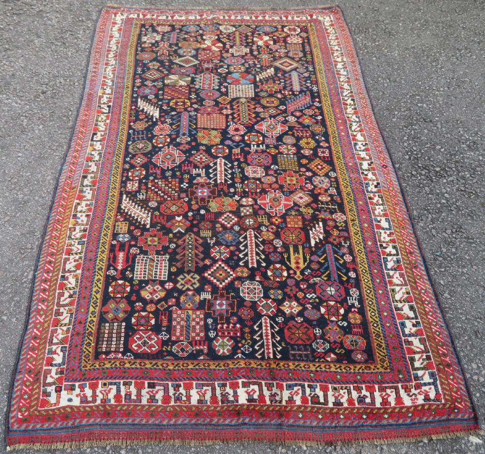 An antique hand-knotted Qashqai wool rug featuring a dark navy field densely filled with geometric tribal motifs and stylised figures within a multi-tiered border. View II