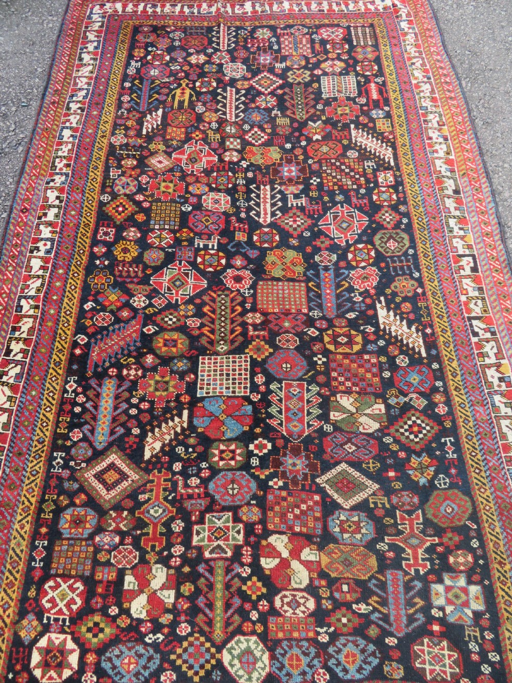 An antique hand-knotted Qashqai wool rug featuring a dark navy field densely filled with geometric tribal motifs and stylised figures within a multi-tiered border. View IV
