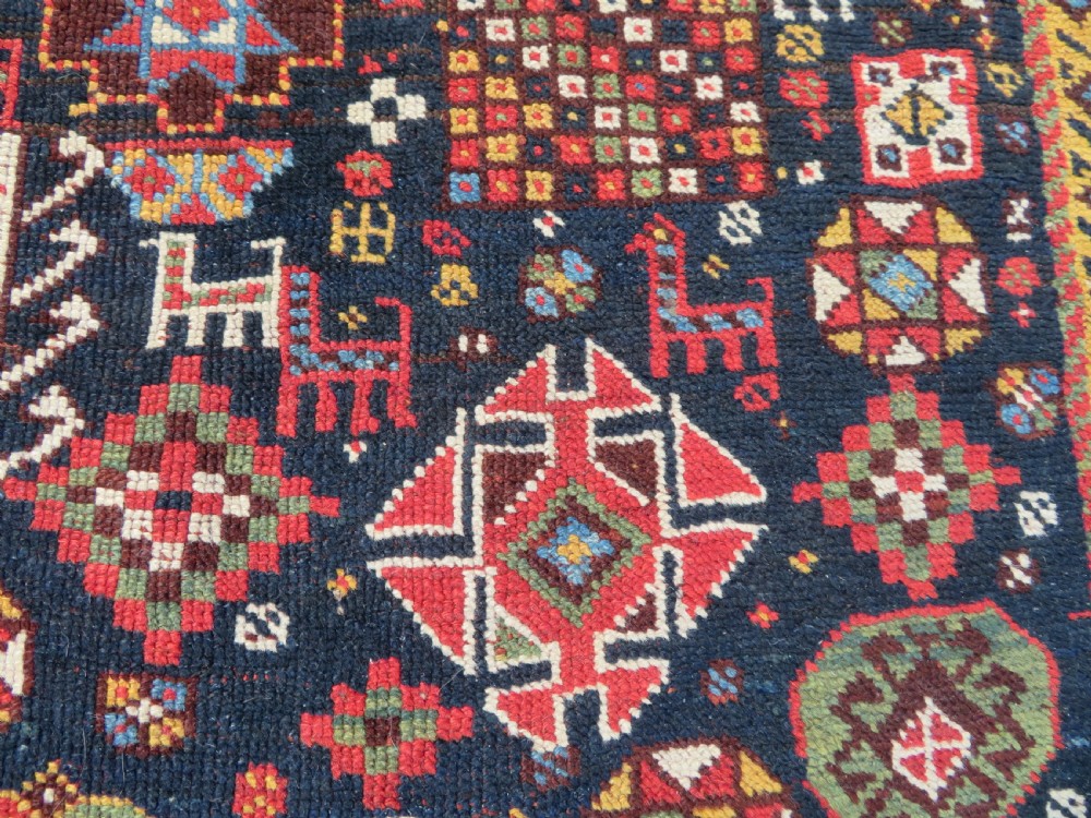 An antique hand-knotted Qashqai wool rug featuring a dark navy field densely filled with geometric tribal motifs and stylised figures within a multi-tiered border. View VI