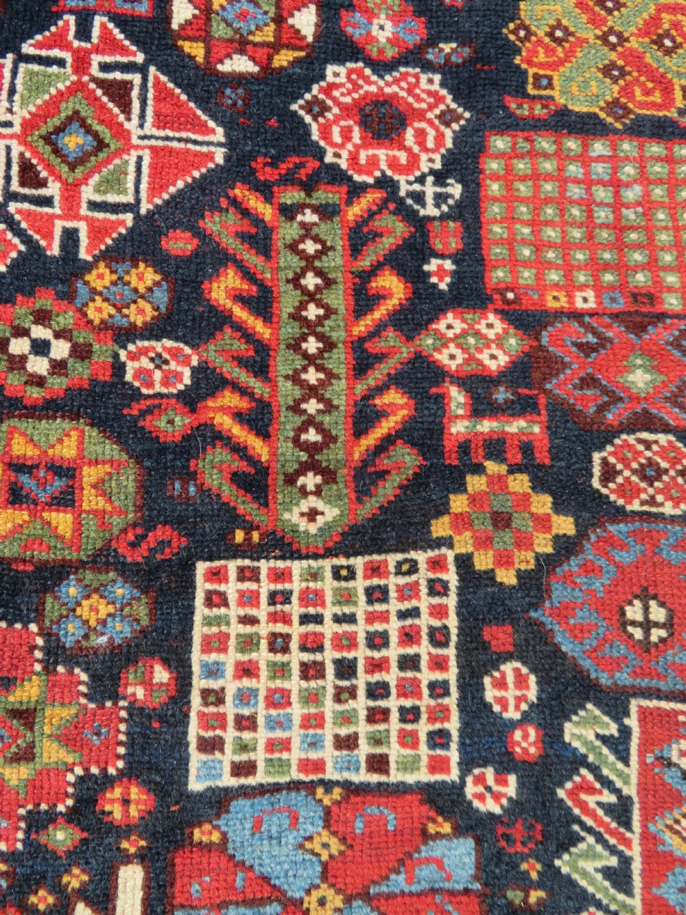 An antique hand-knotted Qashqai wool rug featuring a dark navy field densely filled with geometric tribal motifs and stylised figures within a multi-tiered border. View VII