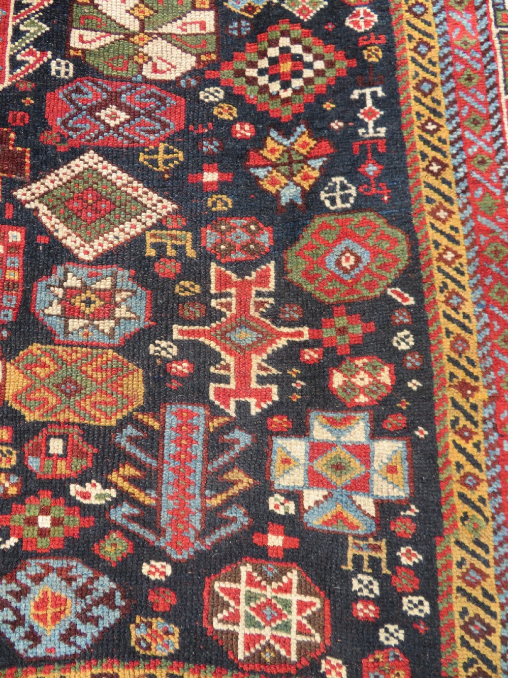 An antique hand-knotted Qashqai wool rug featuring a dark navy field densely filled with geometric tribal motifs and stylised figures within a multi-tiered border. View IX