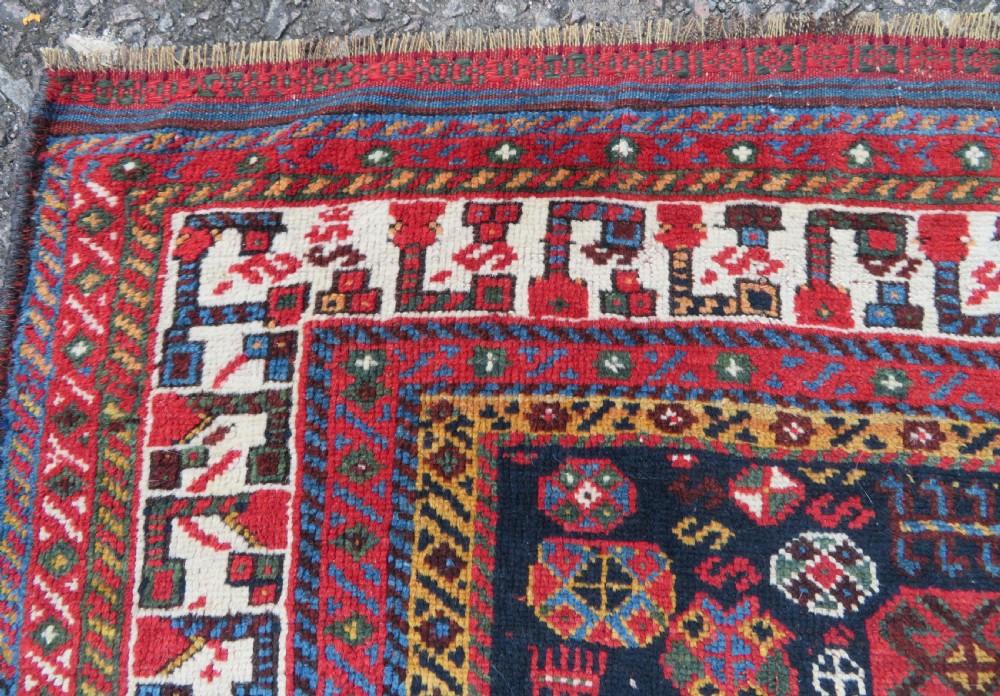 An antique hand-knotted Qashqai wool rug featuring a dark navy field densely filled with geometric tribal motifs and stylised figures within a multi-tiered border. View XV