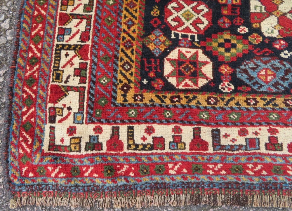An antique hand-knotted Qashqai wool rug featuring a dark navy field densely filled with geometric tribal motifs and stylised figures within a multi-tiered border. View XVIII