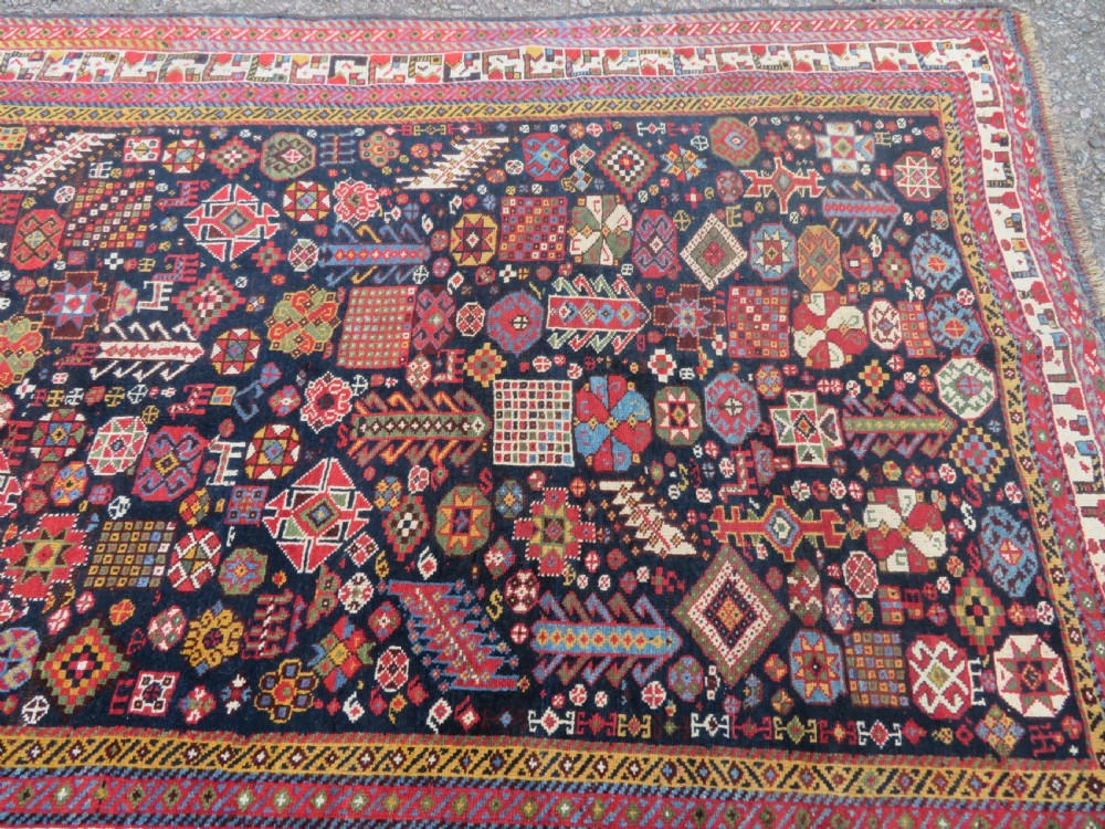 An antique hand-knotted Qashqai wool rug featuring a dark navy field densely filled with geometric tribal motifs and stylised figures within a multi-tiered border. View XX