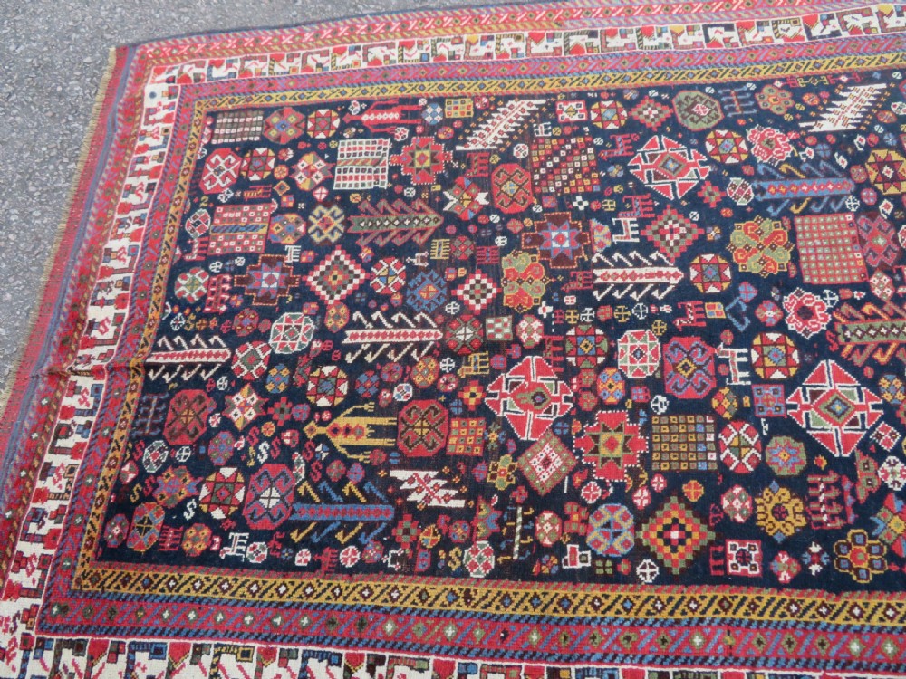 An antique hand-knotted Qashqai wool rug featuring a dark navy field densely filled with geometric tribal motifs and stylised figures within a multi-tiered border. View XXI