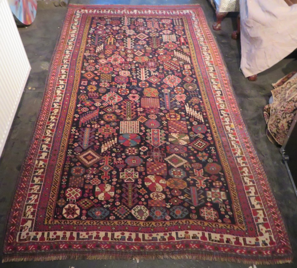 An antique hand-knotted Qashqai wool rug featuring a dark navy field densely filled with geometric tribal motifs and stylised figures within a multi-tiered border. View XXV