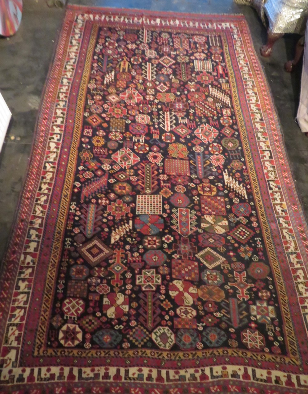 An antique hand-knotted Qashqai wool rug featuring a dark navy field densely filled with geometric tribal motifs and stylised figures within a multi-tiered border. View XXVI