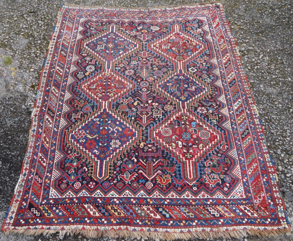 An antique South West Persian Khamseh wool rug with repeating geometric diamond medallions in deep red and indigo blue tones.