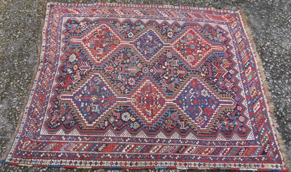 An antique South West Persian Khamseh wool rug with repeating geometric diamond medallions in deep red and indigo blue tones. View II