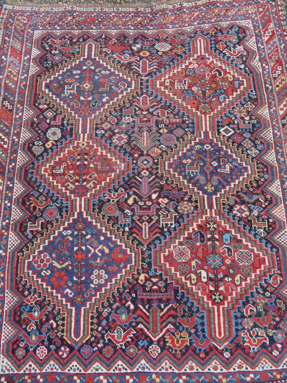 An antique South West Persian Khamseh wool rug with repeating geometric diamond medallions in deep red and indigo blue tones. View III
