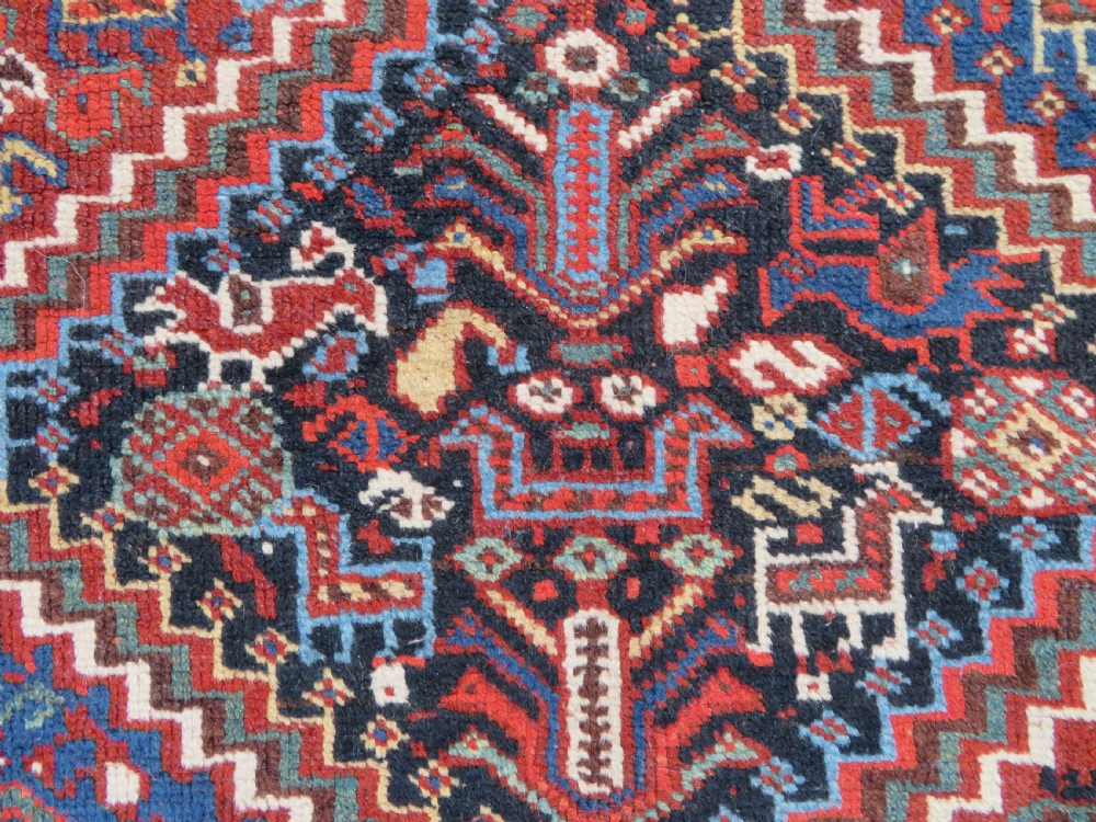 An antique South West Persian Khamseh wool rug with repeating geometric diamond medallions in deep red and indigo blue tones. View IV