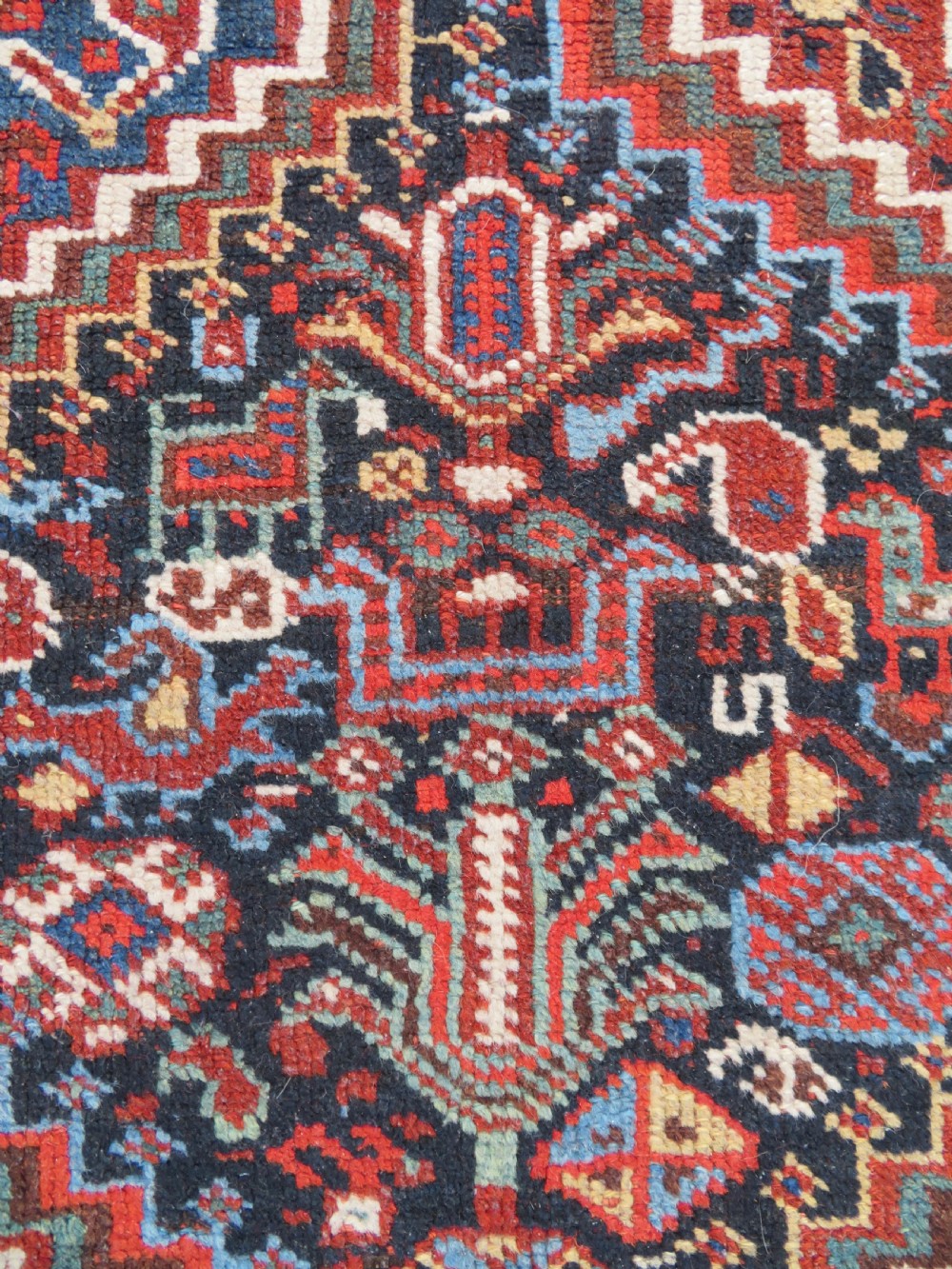 An antique South West Persian Khamseh wool rug with repeating geometric diamond medallions in deep red and indigo blue tones. View V